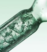 Photographie rapprochée d'une bouteille ou d'un récipient en verre contenant un liquide ou une substance de couleur turquoise tourbillonnant à l'intérieur sur fond blanc.